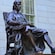 A bronze statue of John Harvard sits with a book on his knee in Harvard Yard